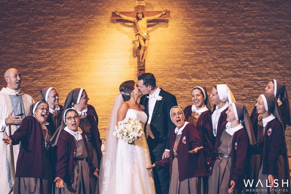 nuns and father looking at bride and groom kiss